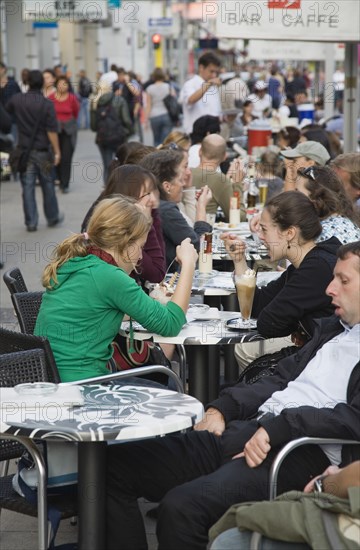 Vienna, Austria. Mariahilf District. Customers at line of busy outside cafe tables. Austria Austrian Republic Vienna Viennese Wien Europe European City Capital Mariahilf District Cafe Outside Outdoor Tables Chairs People Bar Bistro Destination Destinations Osterreich Restaurant Viena Western Europe