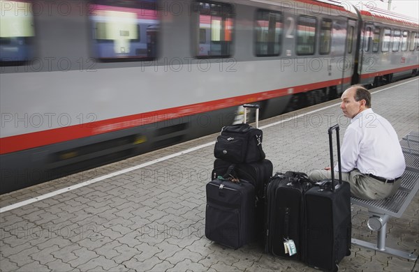 Vienna, Austria. Wien Westbahnhof. Passenger with luggage sitting on Vienna West Station with passing train. Also known as Vienna Western Station this is a major Austrian station and the starting point of the Austrian Western Railway or Westbahn for trains to Salzburg Munich Frankfurt Zurich Budapest Bucharest Belgrad etc. Austria Austrian Republic Vienna Viennese Wien Europe European City Capital Westbahnhof Transport Rail Train Train Station Commuter Tourist Luggage Baggage Bags man Destination Destinations Male Men Guy MŸnchen One individual Solo Lone Solitary Osterreich Sightseeing Tourists Viena Western Europe