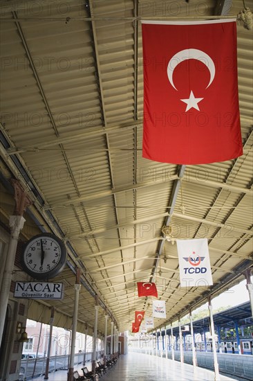 Istanbul, Turkey. Sultanahmet. View along railway platform with Turkish flags hanging from the roof. Istanbul Sirkeci Terminal or Sirkeci GarA is a terminus main station of the Turkish State Railways or TCDD in Sirkeci on the European part of Istanbul. International domestic and regional trains running westwards depart from this station which was inaugurated as the terminus of the Orient Express. Turkey Turkish Istanbul Constantinople Stamboul Stambul City Europe European Asia Asian East West Urban Destination Travel Tourism Transportt Rail Railway Train Trains Station Platform Clock Commuter Sirkeci TCCD Color Destination Destinations Middle East South Eastern Europe Turkiye Western Asia