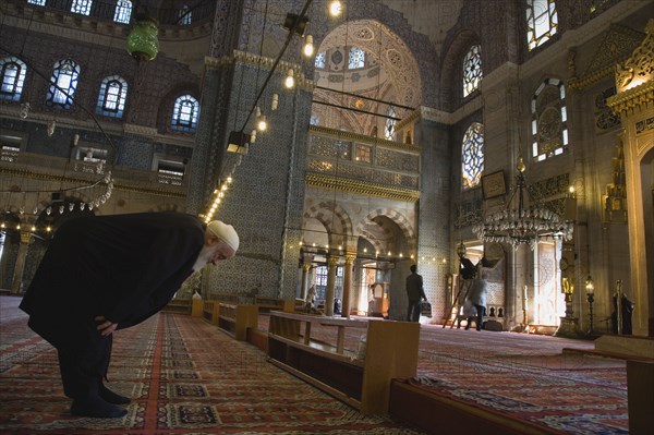 Istanbul, Turkey. Sultanahmet. The New Mosque or Yeni Camii. Tiled and highly decorated interior with elderly man worshipping prayer performing salah or prayer. Turkey Turkish Istanbul Constantinople Stamboul Stambul City Europe European Asia Asian East West Urban Destination Travel Tourism Sultanahmet New Mosque Yeni Camii Interior Muslim Moslem Islam Islamic Religion Religious Prayer Worship Man Salah Worshipping Destination Destinations Male Men Guy Middle East Old Senior Aged One individual Solo Lone Solitary Performance Religion Religious Muslims Islam Islamic South Eastern Europe Turkiye Western Asia