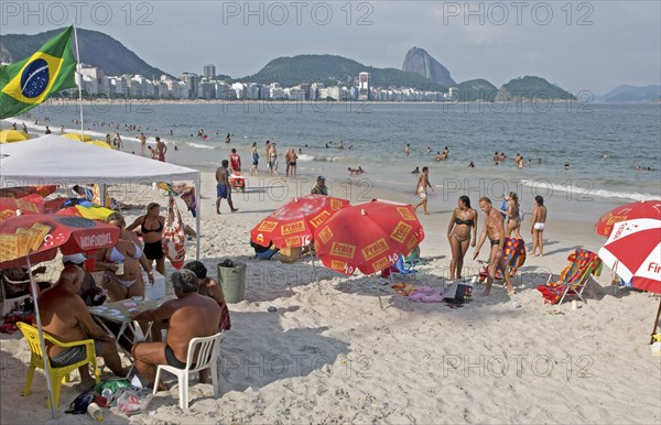 Rio de Janeiro, Brazil. Copacabana beach and Sugarloaf Mountain. Beach umbrellas swimers in sea girls in bikinis and Brazilian flag flying from group in corner. Brazil Brasil Brazilian Brasilian South America Latin Latino American City Travel Destination Urban Vacation Beach Beaches People Sunbathing Crowds Bikini Bikinis Umbrellas Parasols Sugar Loaf Mountain Flag Sand Destination Destinations Holidaymakers Latin America Sand Sandy Beach Tourism Seaside Shore Tourist Tourists Vacation Sand Sandy Beaches Tourism Seaside Shore Tourist Tourists Vacation South America Southern Sunbather Water