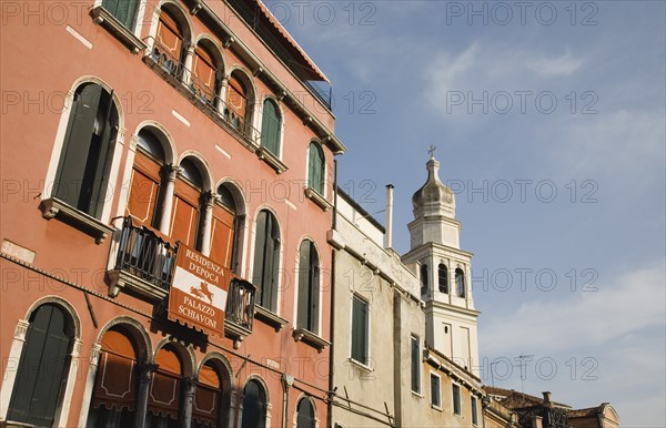 Venice, Veneto, Italy. Centro Storico Restored facade of building painted a terracotta colour with multiple arched windows in late summer sun. Italy Italia Italian Venice Veneto Venezia Europe European City Centro Storico Facade Facade Terracotta Red Arch Arches Arched Window Windows Restored Restoration Palace Palazzo Schivoni Color Destination Destinations Southern Europe