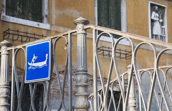 Venice, Veneto, Italy. Centro Storico Gondola access via iron stairway indicated with tourist sign in blue and white. Italy Italia Italian Venice Veneto Venezia Europe European City Centro Storico Sign Bridge Wrought Iron Rail Railings Gondola Blue Destination Destinations Sightseeing Signs Display Posted Signage Southern Europe Tourists