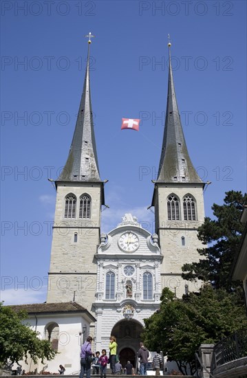 Lucerne, Switzerland. St Leodegar Church exterior with tourists. Switzerland Swiss Lucerne Lucerna Luzern St Saint Leodegar Church Exterior Facade Europe European Urban City Tourist Tourists Tourism Travel People Family Spire Spires Clock Blue Sky Destination Destinations Holidaymakers Religion Religious Schweiz Sightseeing Suisse Svizzera Western Europe