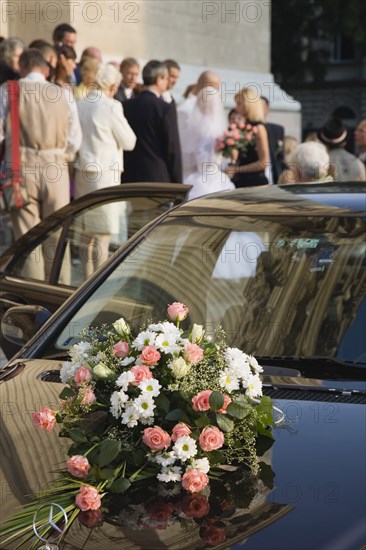 Budapest, Pest County, Hungary. Bride and groom greeting wedding guests on steps of Saint Stephens Basilica with bouquet laid on bonnet of car in foreground. Hungary Hungarian Europe European East Eastern Buda Pest Budapest City People Crowd Couple Wed Wedding Marriage Bride Groom White Dress Veil Flowers St Saint Stephen Stephens Basilica Church Exterior Automobile Automotive Cars Color Cultural Cultures Eastern Europe Hood Marriage Marrying Espousing Hymeneals Nuptials Motorcar Order Fellowship Guild Club Religion Religious