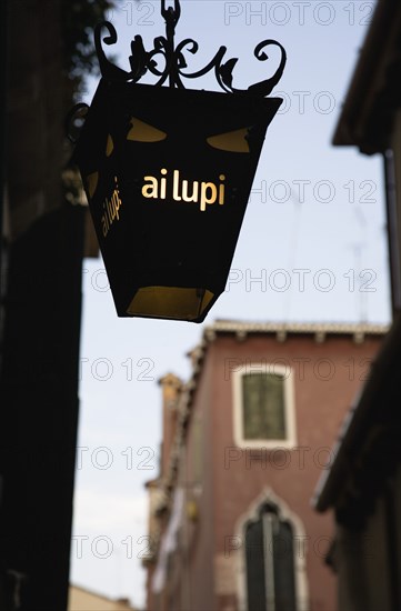 Venice, Veneto, Italy. Centro Storico Lantern outside restaurant inscribed with ai lupi which translates as to the wolves with reference to Dantes use of wolves as metaphor in the Inferno. Italy Italia Italian Venice Veneto Venezia Europe European City Illuminated Sign Restaurant Wolves Ai Lupi Latern Centro Storico Destination Destinations History Historic Signs Display Posted Signage Southern Europe