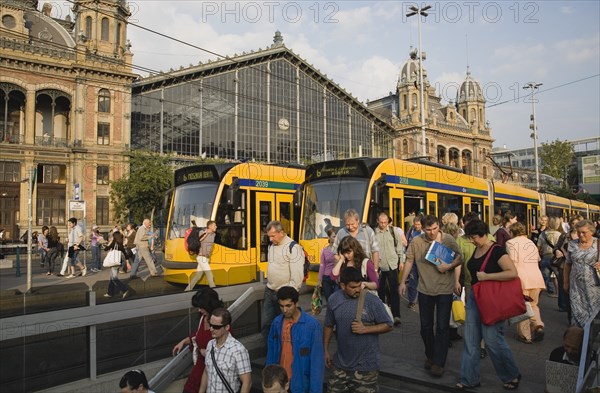 Budapest, Pest County, Hungary. Trams and crowd of passengers in front of rail terminus Budapest Nyugati palyaudvar and walking down steps to metro in foreground with one man turning to look at another who seems to begging on right hand side of steps. Hungary Hungarian Europe European East Eastern Buda Pest Budapest City Transport Rail Train Tram Station Terminus Stop Nyugati Palyaudvar People Crowd Crowded Commuters Tourists Travel Passengers Descend Metro Underground 1 Destination Destinations Eastern Europe Holidaymakers Male Men Guy Roundel Single unitary Tourism