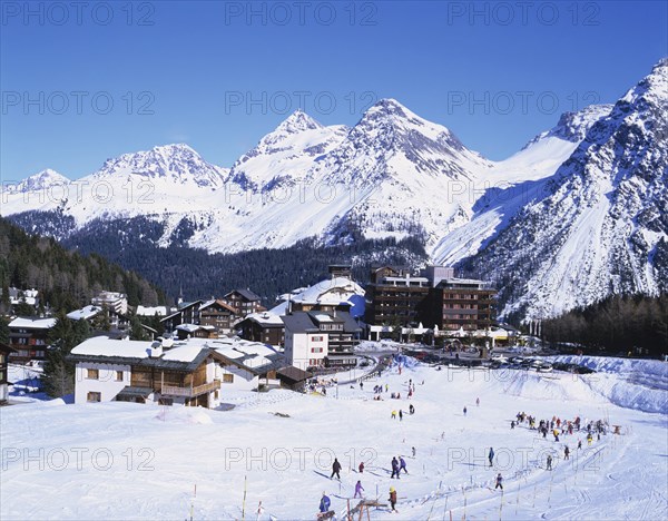 Arosa, Plessur, Switzerland. Ski resort with people skiing in the foreground and the Alps behind. Switzerland Swiss Plessur Graubunden Arosa Resort Europe European Ski Skiing Winter Sport Mountain Mountains Alp Alps Apline tourism tourist Tourists Travel Destination People Group Snow White Blue Sky Color Destination Destinations Holidaymakers Schweiz Sightseeing Suisse Svizzera Western Europe Winter Sport Snow Colour