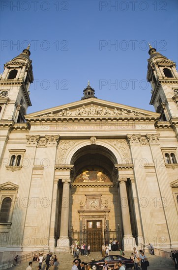 Budapest, Pest County, Hungary. Exterior facade of Saint Stephens Basilica with crowd of visitors on steps at entrance. Hungary Hungarian Europe European East Eastern Buda Pest Budapest City Blue Sky Basilica Stephens Stephen Saint St Facade Facade Christian Religious Religion People Crowd Steps Destination Destinations Eastern Europe Holidaymakers Religion Religious Christianity Christians Tourism Tourist