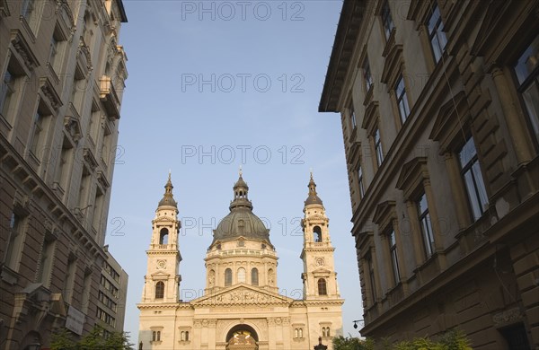 Budapest, Hungary. View along street towards Saint Stephens Basilica exterior facade twin bell towers and central dome. Hungary Hungarian Europe European East Eastern Buda Pest Budapest City Church Architecture Religion Religious Exterior Bell Tower towers Dome Domed Roof Blue Sky St Saint Stephen Stephens Basilica Destination Destinations Eastern Europe