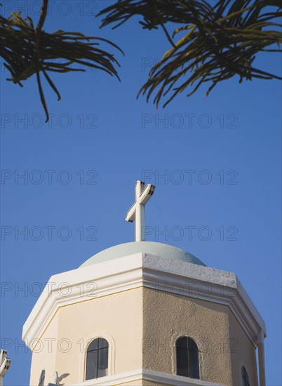 Kos, Dodecanese Islands, Greece. Detail of Greek Orthodox church hexagonal shape with roof dome and cross against blue sky part framed by trees. Greece Greek Europe European Vacation Holiday Holidays Travel Destination Tourism Ellas Hellenic Docecanese Kos Religion Religious Christian Christianity Church Exterior Dome Orthodox Hexagonal Blue Sky Cross Crucifix Destination Destinations Ellada Religion Religious Christianity Christians Southern Europe