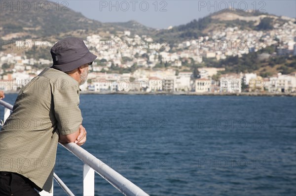 Samos, Northern Aegean, Greece. Vathy. Tourist rests on handrail on deck of ferry between Samos and Kusadasi in Turkey as it leaves Vathy Samos. Greece Greek Europe European Vacation Holiday Holidays Travel Destination Tourism Ellas Hellenic Northern Aegean Samos Island Vathy Tourist Travel Transport Ferry Boat Ship Water Sea Destination Destinations Ellada Holidaymakers Middle East One individual Solo Lone Solitary Sightseeing South Eastern Europe Southern Europe Tourists Turkish Turkiye Water Western Asia