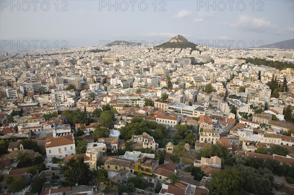 Athens, Attica, Greece. Mount Lycabettus rising in central Athens with densely populated city below part framed by wall in foreground. Greece Greek Europe European Vacation Holiday Holidays Travel Destination Tourism Ellas Hellenic Attica Athens City View Cityscape Aerial Elevated Houses Housing Mount Lycabettus Atenas Athenes Destination Destinations Ellada Southern Europe