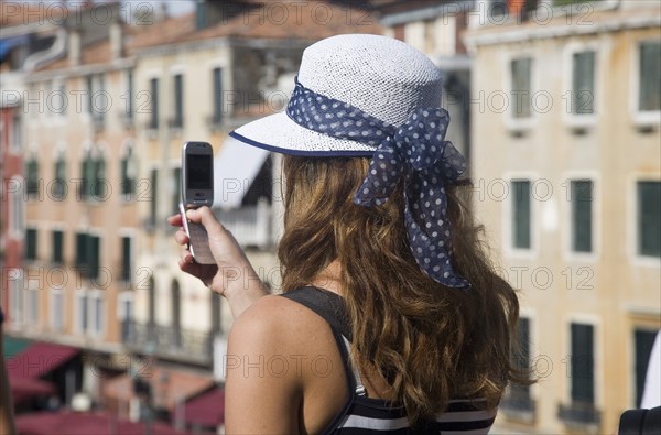 Venice, Veneto, Italy. Young female tourist in white straw hat taking photograph on mobile phone from Rialto bridge looking along Grand Canal. Italy Italia Italian Venice Veneto Venezia Europe European City Grand Canal Camera Phone Mobile Cell Cellphone Taking Picture Snap Snaps Holiday Vacation Tourist Tourists Hat Straw Woman Cellular Destination Destinations Female Women Girl Lady Holidaymakers Immature One individual Solo Lone Solitary Sightseeing Southern Europe Tourism