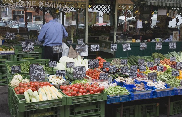 Vienna, Austria. The Naschmarkt. Stallholder standing behind and with back to display of fresh produce including tomatoes sweetcorn aubergine and mushrooms. Austria Austrian Republic Vienna Viennese Wien Europe European City Capital Naschmarkt Market Display Fresh Food Fruit Vegetables Veg Vegetable Stall Shop Store Destination Destinations One individual Solo Lone Solitary Osterreich Viena Western Europe