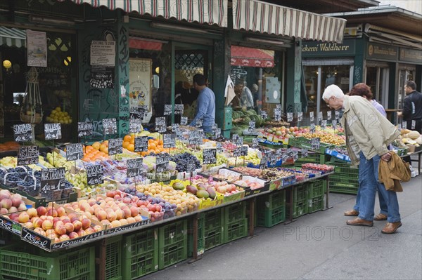 Vienna, Austria. The Naschmarkt. Customers at fresh produce stall looking at display that includes peaches nectarines plums and grapes. Austria Austrian Republic Vienna Viennese Wien Europe European City Capital Naschmarkt Market Display Fresh Food Fruit Vegetables Veg Vegetable Stall Shop Store Destination Destinations Osterreich Viena Western Europe