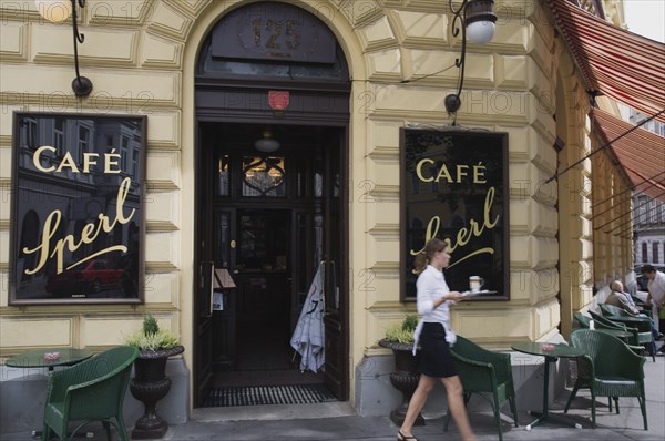 Vienna, Austria. Mariahilf District. Cafe Sperl the preferred cafe of Adolf Hitler. Exterior facade with waitress carrying coffee order out to customers at outside tables beneath striped awning. In warmer months customers can often sit outside in a Schanigarten Austria Austrian Vienna Viennese Wien Mariahlf 6th District Cafe Sperl Hitler Waitress Entrance Coffee Exterior Europe European Work Urban City Table Tables Schanigarten Bar Bistro Destination Destinations History Historic Osterreich Restaurant Viena Western Europe