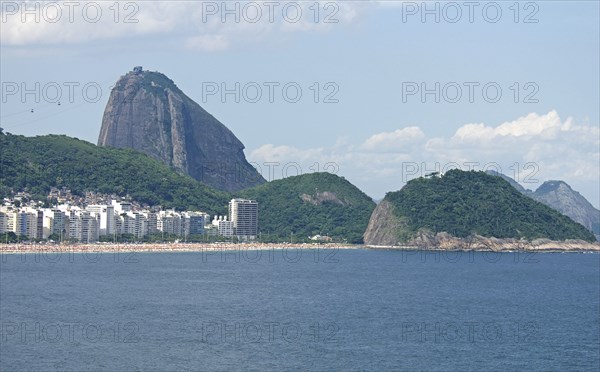 Rio de Janeiro, Brazil. Copacabana beach. Hotels and crowds on the beach in the distance blue sea and sky with puffy white clouds cable car to the top of Sugarloaf Mountain beyond. Brazil Brasil Brazilian Brasilian South America Latin Latino American City Travel Destination Urban Vacation Beach Beaches People Sunbathing Crowds rio de Janeiro Copacabana Hotels Sugarloaf Mountain Sugar Loaf Cable Car Cablecar Automobile Automotive Cars Destination Destinations Holidaymakers Latin America Motorcar Sand Sandy Beach Tourism Seaside Shore Tourist Tourists Vacation Sand Sandy Beaches Tourism Seaside Shore Tourist Tourists Vacation Scenic South America Southern Sunbather Water