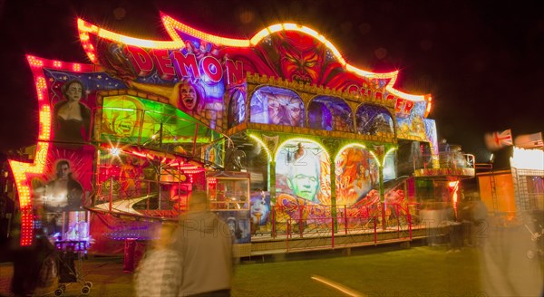 Lancing, West Sussex, England. Entertainment Funfairs Rides illuminated at night. England English UK United Kingdom GB Great Britain British Europe European West Sussex Lancing Funfair Rides Night Entertainment Leisure Color Colour Colorful Colourful Colored Coloured People Crowd Blur Blurred Ferris Wheel Big Neon Light