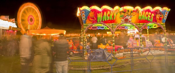 Lancing, West Sussex, England. Entertainment Funfairs Rides illuminated at night. England English UK United Kingdom GB Great Britain British Europe European West Sussex Lancing Funfair Rides Night Entertainment Leisure Color Colour Colorful Colourful Colored Coloured People Crowd Blur Blurred Ferris Wheel Big Neon Light