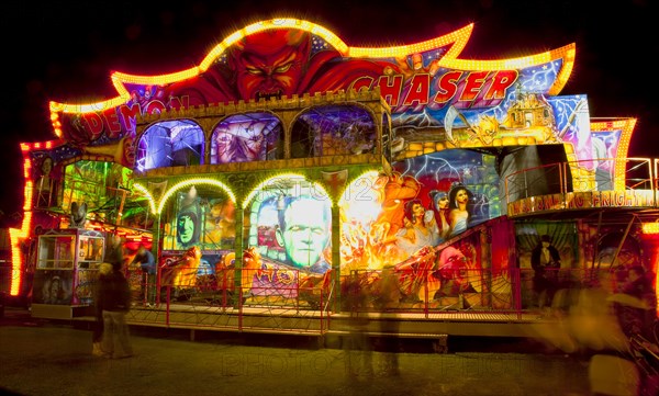 Lancing, West Sussex, England. Entertainment Funfairs Rides illuminated at night. England English UK United Kingdom GB Great Britain British Europe European West Sussex Lancing Funfair Rides Night Entertainment Leisure Color Colour Colorful Colourful Colored Coloured People Crowd Blur Blurred Ferris Wheel Big Neon Light