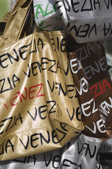 Venice, Veneto, Italy. Shopping bags on souvenir stall for sale opposite St Marks Square in the sunshine. Italy Italia Italian Venice Veneto Venezia Europe European City Bag Bags Handbag Handbags Market Markets Leather Gold Silver Writing Destination Destinations Shops Shoppers Mall Retail Buy Buying Market Markets Southern Europe