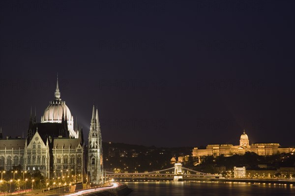 Budapest, Hungary. View along the River Danube at night with the Parliament building on the left the Chain Bridge and the Royal Palace on the right all illuminated brightly. Hungary Hungarian Europe European East Eastern City Cityscape Skyline Night Nighttime Dark Lights Lit Illuminated River Danube Parliament Royal Palace Chain Bridge Travel Destination Holiday Vacation Break Buda Pest Budapest Citiscape Building Buildings Urban Architecture Destination Destinations Eastern Europe Nite Parliment