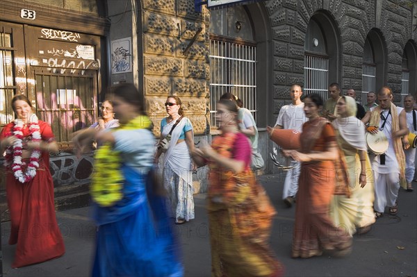 Budapest, Pest County, Hungary. Hare Krishna devotees singing and dancing on Andrassy UtIn Pest with graffiti covered doorway behind. The International Society for Krishna Consciousness or ISKCON also known as the Hare Krishna movement is a Hindu Vaishnava religious organization. Hungary Hungarian Europe European East Eastern Buda Pest Budapest City Religion religious Hare Krishna Hindu Hinduism Vaishnava Women Women Female Worship Worhippers Dance Dancing Dancers Sing Singing Movemnet Blurred Eastern Europe Female Woman Girl Lady Order Fellowship Guild Club Religion Religious Hinduism Hindus