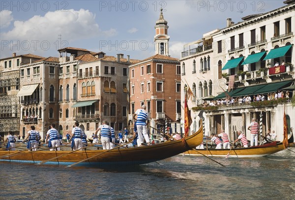 Venice, Veneto, Italy. Participants in the Regata Storico historical Regatta held annually in September wearing traditional costume and approaching the Rialto bridge with onlookers gathered on the balconies of canalside buildings behind. Teams represent Sestiere districts of Venice in traditional races. Italy Italia Italian Venice Veneto Venezia Europe European City Regata Regatta Gondola Gondola Gondolas Gondolier Boat Architecture Exterior Classic Classical Destination Destinations History Historic Holidaymakers Older Southern Europe Tourism Tourist