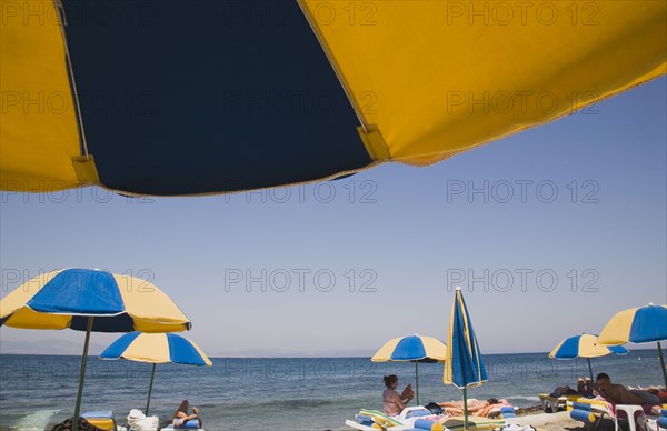 Kos, Dodecanese Islands, Greece. Sunbathers on loungers underneath yellow and blue striped beach parasols on beach outside kos Town. Greece Greek Europe European Vacation Holiday Holidays Travel Destination Tourism Ellas Hellenic Docecanese Tigaki Beach Sun Sunbathers Sunbathers Sunbathing Tourists Tourists Umbrellas Parasols Sea Color Destination Destinations Ellada Holidaymakers Sand Sandy Beaches Tourism Seaside Shore Tourist Tourists Vacation Southern Europe Water