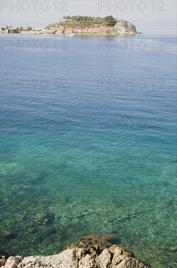 Kusadasi, Aydin Province, Turkey. View towards Guvercin Ada or Pigeon Island across clear turquoise water. Turkey Turkish Eurasia Eurasian Europe Asia Turkiye Aydin Province Kusadasi Guvercin Ada Pigeon Island Sea Water Clear Turquoise Blue Green Color Destination Destinations European Middle East Scenic South Eastern Europe Water Western Asia