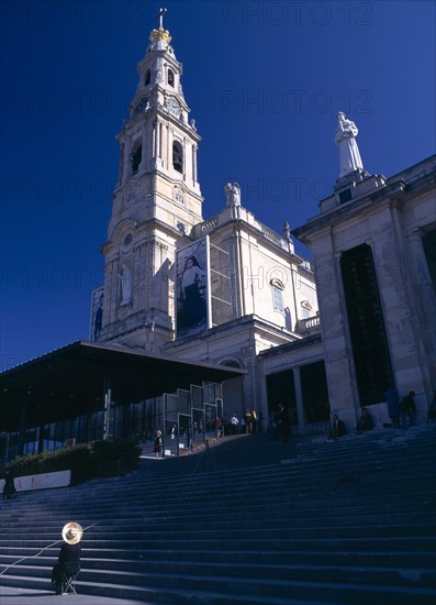 Fatima, Beira Litoral, Portugal. Woman wearing hat seated by steps beneath the church Female Women Girl Lady Portuguese Religion Southern Europe