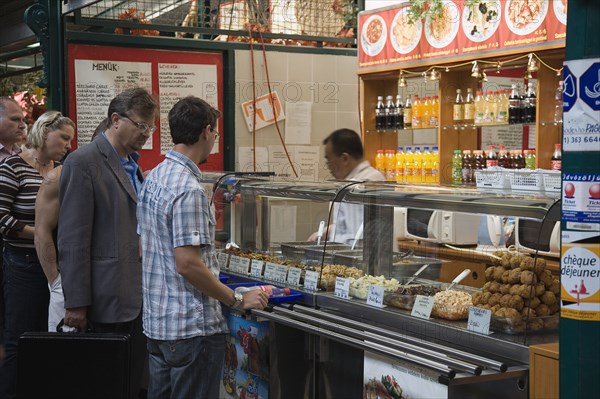 Budapest, Pest County, Hungary. Queue of customers at stall selling snacks salads and other dishes at Nagy Vasarcsarnok the Central Market. Hungary Hungarian Europe European East Eastern Buda Pest Budapest City Market markets Central Nagy Vasarcsarnok Food Snacks Fast Drinks Soft Soda Pop Customers Queue Queuing Line Destination Destinations Eastern Europe