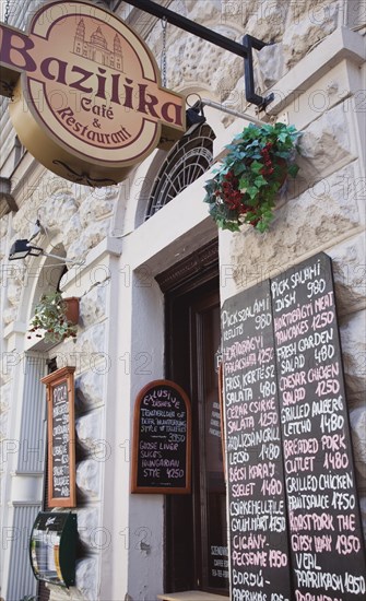 Budapest, Pest County, Hungary. Bazilika Cafe and Restaurant exterior with hanging sign and menu boards in Hungarian and English near Saint Stephens Basilica. Hungary Hungarian Europe European East Eastern Buda Pest Budapest City Cafe restaurant Food Bazilika Entrance Signs Menu Boards Bar Bistro Destination Destinations Eastern Europe Signs Display Posted Signage