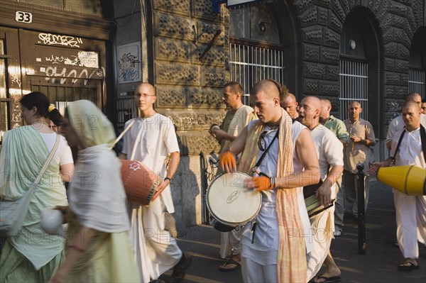 Budapest, Pest County, Hungary. Hare Krishna devotees singing and dancing on Andrassy UtIn Pest with graffiti covered doorway behind. The International Society for Krishna Consciousness or ISKCON also known as the Hare Krishna movement is a Hindu Vaishnava religious organization. Hungary Hungarian Europe European East Eastern Buda Pest Budapest City Religion religious Hare Krishna Hindu Hinduism Vaishnava Women Women Female Worship Worhippers Dance Dancing Dancers Sing Singing Men Male Man Playing Drum Drums Eastern Europe Female Woman Girl Lady Male Man Guy Male Men Guy Order Fellowship Guild Club Religion Religious Hinduism Hindus