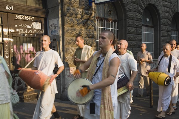 Budapest, Pest County, Hungary. Hare Krishna devotees singing and dancing on Andrassy UtIn Pest with graffiti covered doorway behind. The International Society for Krishna Consciousness or ISKCON also known as the Hare Krishna movement is a Hindu Vaishnava religious organization. Hungary Hungarian Europe European East Eastern Buda Pest Budapest City Religion religious Hare Krishna Hindu Hinduism Vaishnava Women Women Female Worship Worhippers Dance Dancing Dancers Sing Singing Man Men Male Drum Drums Drummer Drummers Drumming Music Eastern Europe Female Woman Girl Lady Male Man Guy Male Men Guy Order Fellowship Guild Club Religion Religious Hinduism Hindus