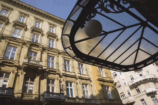 Budapest, Pest County, Hungary. Art Nouveau era apartment exterior facades with part seen underside of decorative metal and glass roof in foreground. Hungary Hungarian Europe European East Eastern Buda Pest Budapest City Architecture Apartment Apartments Buildings Buildings Exterior Facade Art Nouveau Destination Destinations Eastern Europe Flat