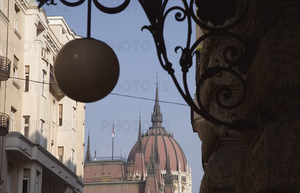 Budapest, Pest County, Hungary. Art Nouveau era apartment facades with domed roof of Hungarian Parliament Building behind and decorative metalwork and hanging spherical light in foreground. Hungary Hungarian Europe European East Eastern Buda Pest Budapest City Architecture Apartment Apartments Exteriors Exterior Facade Facades Nouveau Art Lamp Light Blue Destination Destinations Eastern Europe Flat Parliment