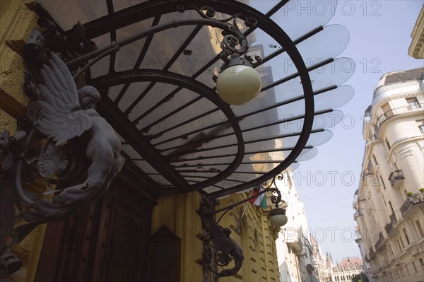 Budapest, Pest County, Hungary. Art nouveau building facade and apartment entrance with decorative metalwork and glass screen above door. Hungary Hungarian Europe European East Eastern Buda Pest Budapest City Apartment Apartments Apartments Flats Exterior Facade Art Nouveau Lamp Light Ornate Ironwork Glass Iron Screen Awning Canopy Destination Destinations Eastern Europe Flat