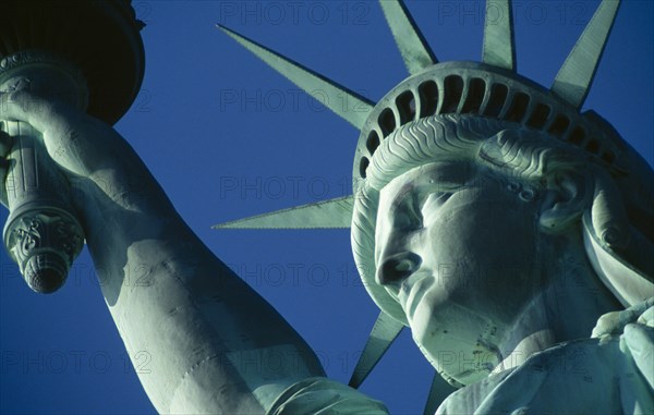 New York City, New York State, USA. The Statue of Liberty. Detail of head and arm holding torch against a blue sky. American Color Destination Destinations North America Northern Sightseeing Tourists United States of America Colour Holidaymakers Tourism