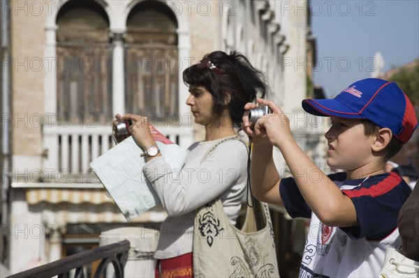 Venice, Veneto, Italy. Mother and son take photographs of canal view opposite St. Marks. Italy Italia Italian Venice Veneto Venezia Europe European City Tourist Tourists Woman Boy Young Camera Cameras Photograph Picture Pictures Photographs Snaps Digital Destination Destinations Female Women Girl Lady Holidaymakers Immature Kids Mum Sightseeing Southern Europe Tourism