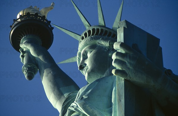 New York City, New York State, USA. The Statue of Liberty. Detail of head and arm holding torch against a blue sky. American Color Destination Destinations North America Northern Sightseeing Tourists United States of America Colour Holidaymakers Tourism