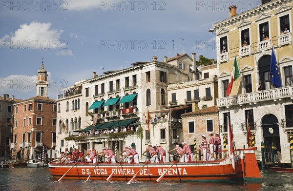 Venice, Veneto, Italy. Participants in the Regata Storico historical Regatta held annually in September wearing traditional costume approaching the Rialto bridge with onlookers gathered on the balconies of canalside buildings behind. Teams represent Sestiere districts of Venice in traditional races. Italy Italia Italian Venice Veneto Venezia Europe European City Regata Regatta Gondola Gondola Gondolas Gondolier Boat Architecture Exterior Water Classic Classical Destination Destinations History Historic Holidaymakers Older Southern Europe Tourism Tourist