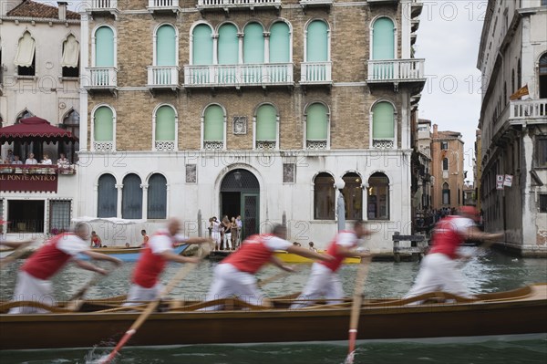 Venice, Veneto, Italy. Participants in the Regata Storico historical Regatta held annually in September in blur of motion as they approach the Rialto bridge passing canalside buildings with onlookers gathered on balconies. Teams represent Sestiere districts of Venice in traditional races. Italy Italia Italian Venice Veneto Venezia Europe European City Regata Regatta Gondola Gondola Gondolas Gondolier Boat Architecture Exterior Water Classic Classical Destination Destinations History Historic Holidaymakers Older Southern Europe Tourism Tourist