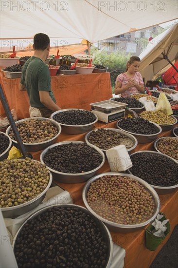 Kusadasi, Aydin Province, Turkey. Stall at weekly market selling olives and nuts with male stallholderand young girl standing behind display and set of electronic scales. Turkey Turkish Eurasia Eurasian Europe Asia Turkiye Aydin Province Kusadasi Market Markets Stall Display Olive Olives Dried Nut Nuts Scales Electronic Multi Muliple Color Colour Colors Colours Colored Coloured Destination Destinations European Immature Kids Middle East South Eastern Europe Western Asia