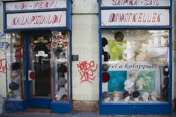 Budapest, Pest County, Hungary. Graffiti on hat shop facade around window display. Hungary Hungarian Europe European East Eastern Buda Pest Budapest City Hat Milliner Hats Shop Store Architecture Facade Entrance Door Window Display Graffiti Graffito Destination Destinations Eastern Europe Ecology Entorno Environmental Environnement Green Issues