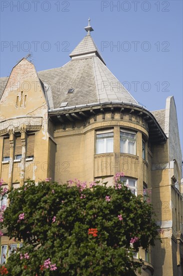 Budapest, Pest County, Hungary. Part view of Empire era apartment blocks with baskets of pink geraniums in foreground. Hungary Hungarian Europe European East Eastern Buda Pest Budapest City Home Housing Flats Flats Apartment Sky Blue Geraniums Flowers Basket Hanging Facade Exterior Detail Destination Destinations Eastern Europe Flat