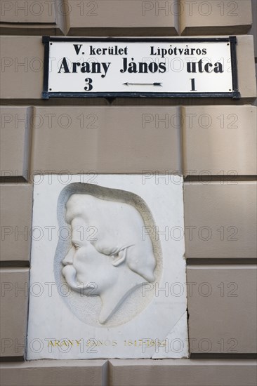 Budapest, Pest County, Hungary. Street sign and relief portrait of Janos Arany 1817 to 1882 the Hungarian journalist writer poet and translator known as the Shakespeare of ballads whose most famous work was the Toldi trilogy. Hungary Hungarian Europe European East Eastern Buda Pest Budapest City Architecture Details Facade Art Sculpture Carving Relief Janos Arany Sign Cultural Cultures Destination Destinations Eastern Europe Order Fellowship Guild Club Signs Display Posted Signage