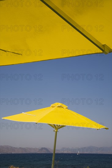 Kos, Dodecanese Islands, Greece. Bright yellow parasols on beach outside Kos Town view towards distant coastline beyond. Greece Greek Europe European Vacation Holiday Holidays Travel Destination Tourism Ellas Hellenic Docecanese Kos Sea Sea Umbrella Umbrellas Parasol Parasols Yellow Blue Color Destination Destinations Ellada Sand Sandy Beaches Tourism Seaside Shore Tourist Tourists Vacation Southern Europe Water