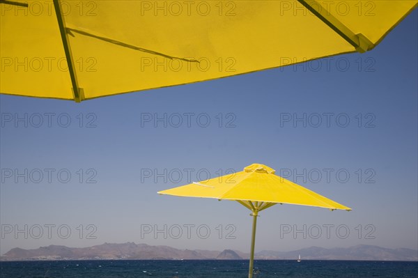 Kos, Dodecanese Islands, Greece. Bright yellow parasols on beach outside Kos Town with view towards distant coastline beyond. Greek Europe European Vacation Holiday Holidays Travel Destination Tourism Ellas Hellenic Docecanese Kos Beach Sea Umbrella Umbrellas Parasol Parasols Yellow Blue Color Destination Destinations Ellada Sand Sandy Beaches Tourism Seaside Shore Tourist Tourists Vacation Southern Europe Water